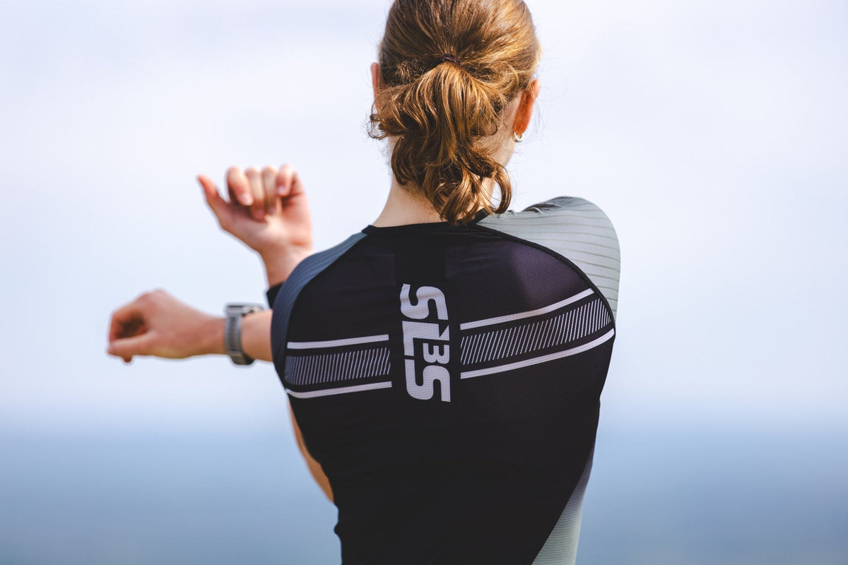 Triathlete in SLS3 triathlon apparel running beside a lake on a sunny day.