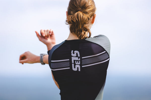 Triathlete in SLS3 triathlon apparel running beside a lake on a sunny day.